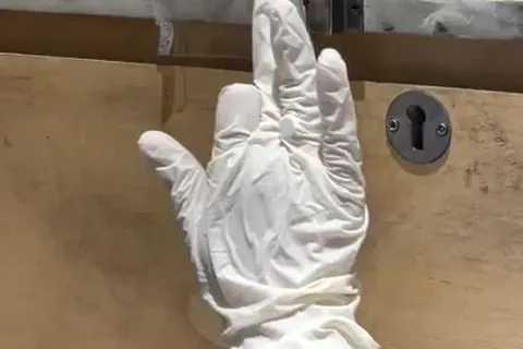 Gloved examiner lifting prints near a drawer lock after a theft